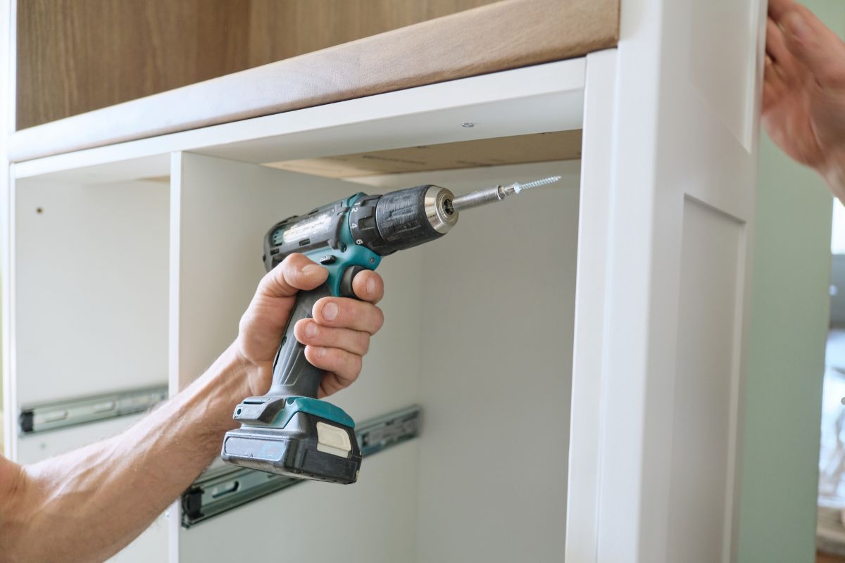 A man drills into a wall to install a cabinet, preparing the area for furniture repair and ensuring proper support.