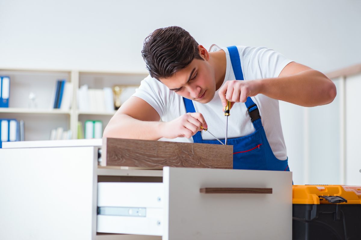 A man in an apron repairs a cabinet, demonstrating skills in furniture restoration and upholstery repair services. 